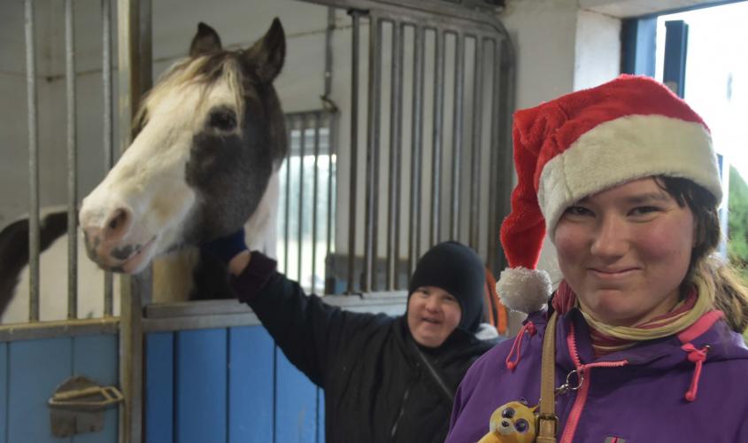 Flicka med tomteluva står med häst i stallet.